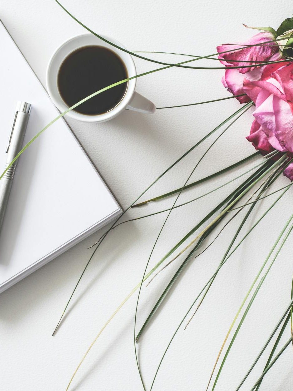 red rose flowers bouquet on white surface beside spring book with click pen and cup of cofffee